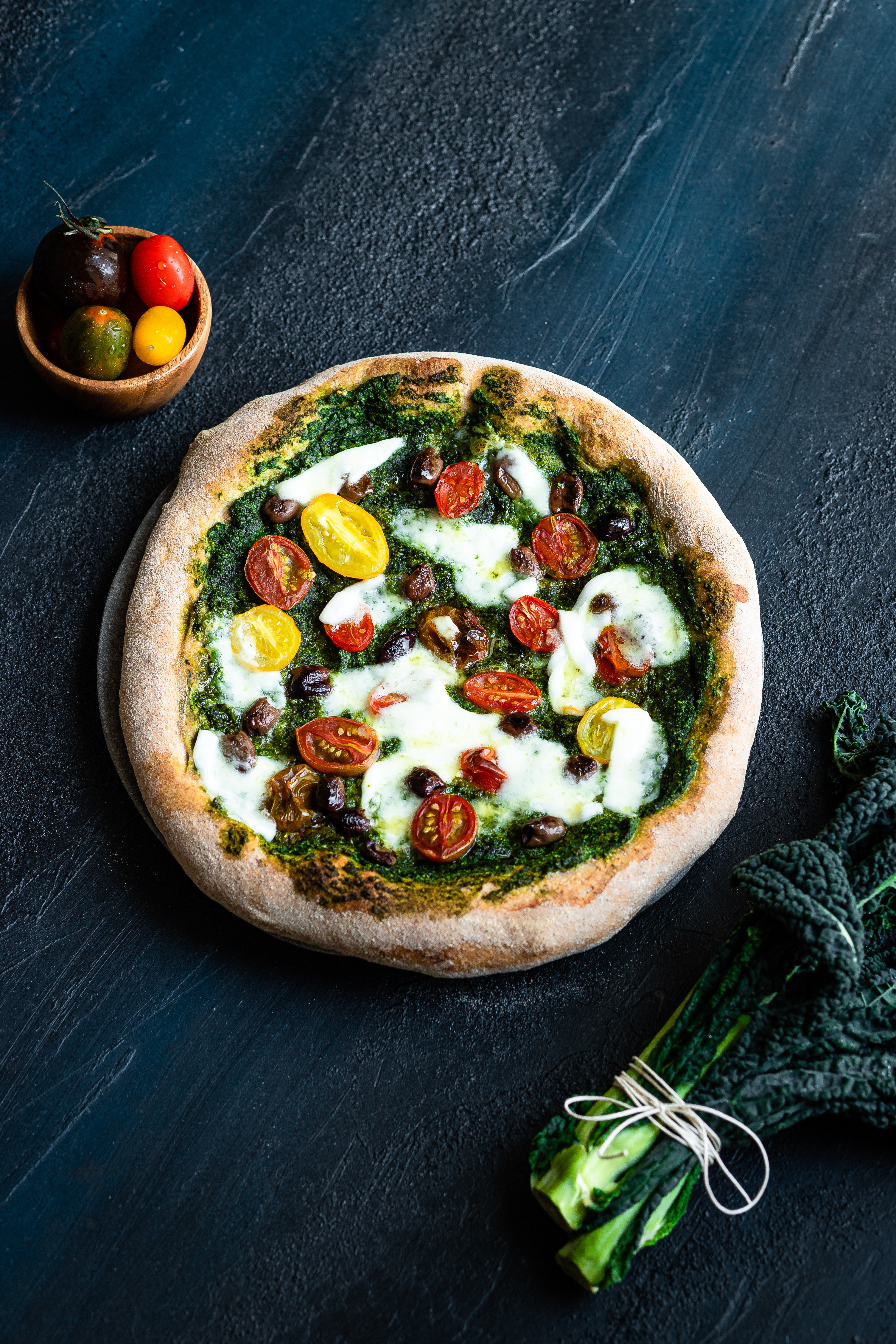 Pizza integrale con pesto di cavolo nero, pomodorini, olive taggiasche e  mozzarella di bufala